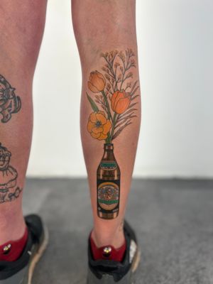 Get a uniquely designed tattoo by Paula featuring a beautiful bouquet of flowers alongside a beer bottle, perfect for those who enjoy floral and beverage motifs.
