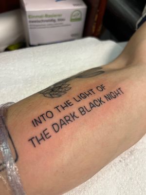 Get inspired by this stunning small lettering tattoo featuring the quote 'into the light of the dark black night' by Claudia Vicente.