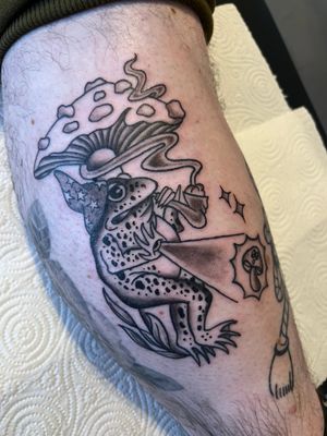 Get a magical tattoo by Claudia Vicente combining a frog, wizard, and mushroom in illustrative traditional style.