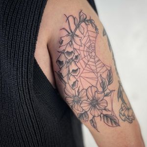 Get a stunning illustrative tattoo of flowers, plants, and a spider web designed by Paula for a unique and beautiful piece of body art.