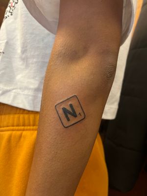 Unique illustrative tattoo featuring nitrogen element symbol from the chemical table, expertly done by Claudia Vicente.