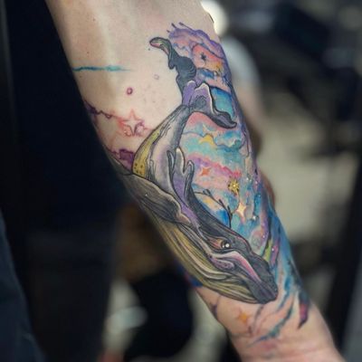 Get lost in the cosmic depths with this stunning neo-traditional watercolor tattoo featuring a majestic whale swimming among the stars. By artist Holly Valley.