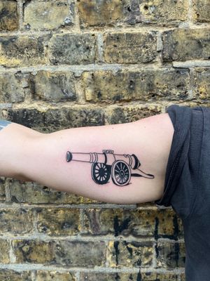 Get a sleek illustrative cannon tattoo by artist Dave Norman, showcasing a minimalist design inspired by an arsenal.