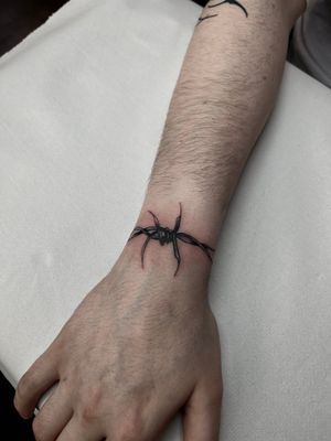 Get edgy with this blackwork illustrative tattoo featuring barbed wire and thorns by the talented artist Dominga Longo.