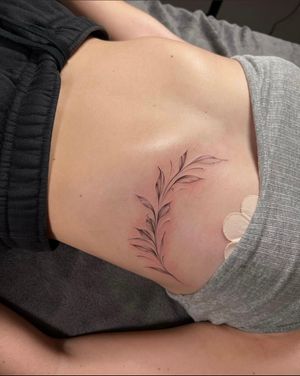 Elegant flower, twig, and leaf design by Ion Caraman for a delicate and stunning under-boob tattoo.
