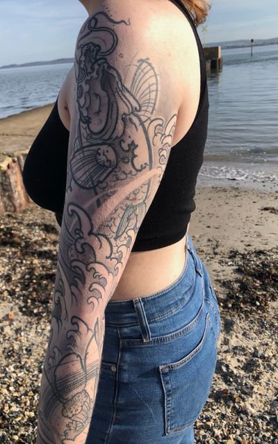 Experience the beauty of black & gray waves and koi fish in this intricate illustrative tattoo by artist Hannah Keuls.