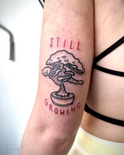 Get a unique small lettering and illustrative tattoo of a bonsai tree symbolizing growth and resilience, done by the talented artist Ben Twentyman.