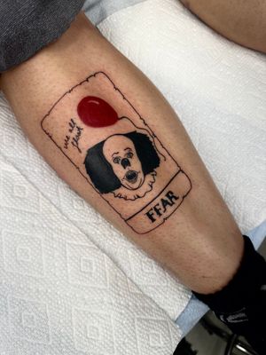 Get a spooky and minimalist tattoo with small lettering of Pennywise from IT on a playing card, by Miss Vampira.