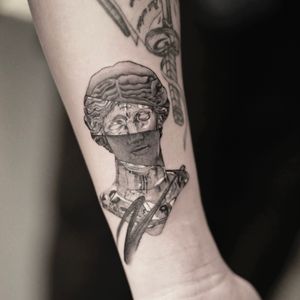 Get mesmerized by Gloria Gu's black and gray surrealistic tattoo featuring a chrome statue motif.