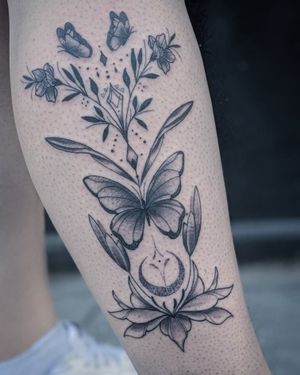 An intricate dotwork and fine line tattoo featuring a beautiful moon, butterflies, flowers, and plants, by the talented artist Nat.