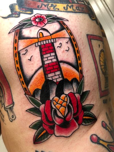 Get inked with this stunning traditional tattoo featuring a vibrant peony intertwined with a majestic lighthouse. Designed by the talented artist Angel Face.