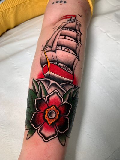 Sail away with this stunning traditional tattoo by Angel Face featuring a beautiful flower intertwined with a majestic ship design.