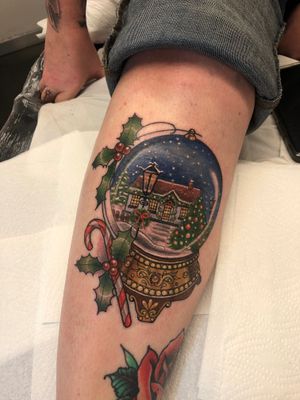 Get in the holiday spirit with this festive snowglobe tattoo featuring a candy cane motif, by Elena Mameri. Perfect for Christmas lovers!