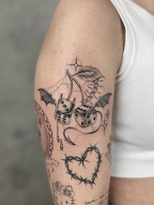 Illustrative black and gray tattoo by Laura May featuring metallic dice, cherry, and devil motif in dotwork style.