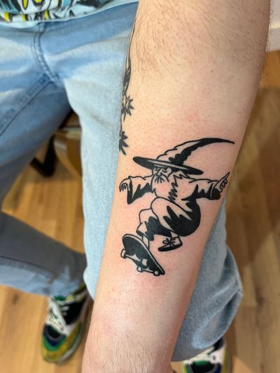 Get a cool blackwork tattoo of a wizard skating, designed by renowned artist Dave Norman. Ignite your inner magic with this unique design.