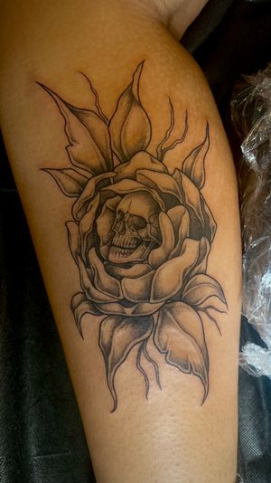 This unique dotwork tattoo combines a delicate flower with a haunting skull illustration, expertly executed by renowned artist Kat Jennings.