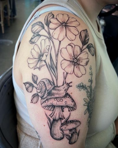 Explore the beauty of nature with this stunning tattoo featuring a snail, mushroom, and flowers, designed by Hannah Senoj.