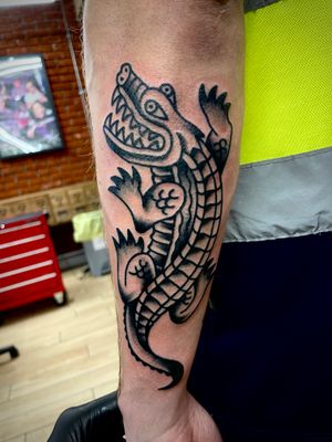 Get a fierce and timeless traditional tattoo of an alligator by the talented artist Goblyn Crew. Perfect for those who love bold designs.