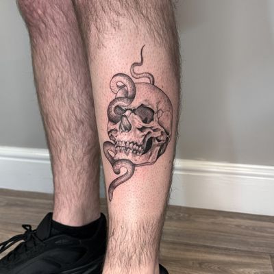 Immerse yourself in the intricate details of this black and gray, dotwork masterpiece featuring a snake intertwined with a skull, expertly executed by tattoo artist Tas Kal.