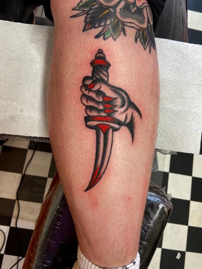 Get inked with a striking traditional tattoo featuring a dagger and hand motif by flashbyaj. Timeless and bold design!