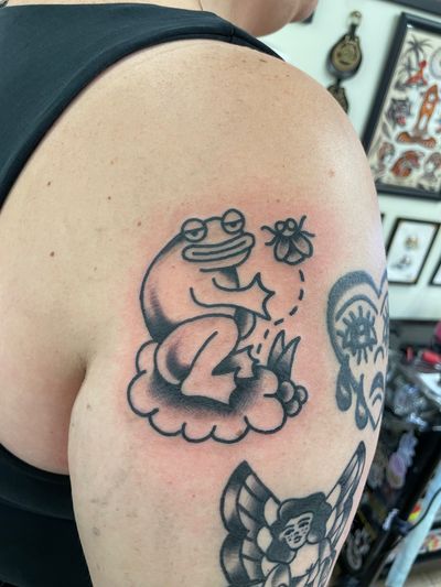 Get a classic tattoo featuring a frog and fly in traditional style by the talented artist, Goblyn Crew.