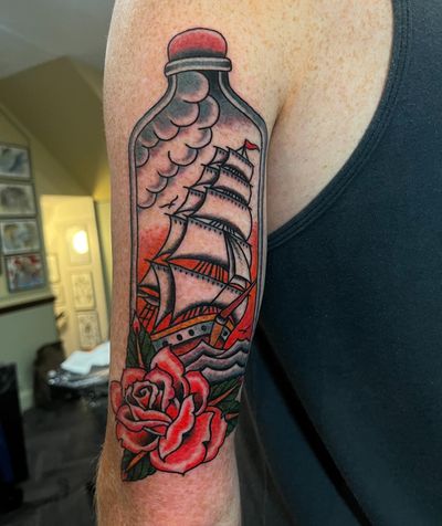 Get inked by Barney Coles with this unique illustrative traditional tattoo featuring a rose, ship, and bottle design.