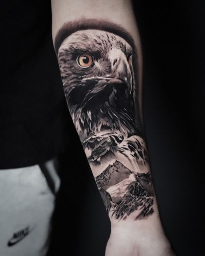 Black and gray tattoo by Milan Boros featuring a majestic eagle flying over a scenic mountain landscape.