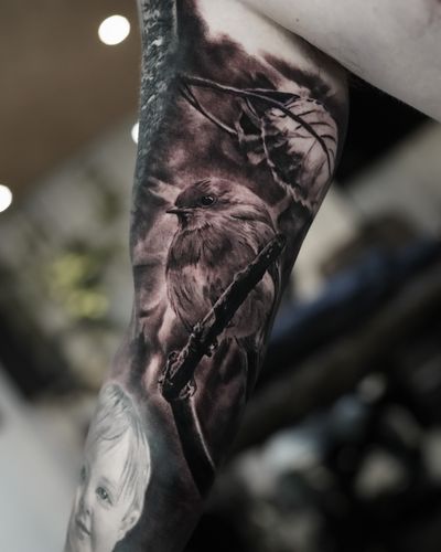 Stunning black and gray tattoo by Milan Boros featuring a lifelike bird perched on a tree branch, showcasing intricate details and blending seamlessly into nature.