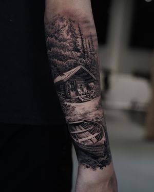Immerse yourself in nature with this stunning black and gray tattoo featuring a cabin by the lake surrounded by a lush forest. By tattoo artist Milan Boros.