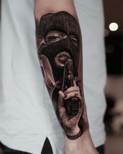 Captivating black and gray tattoo featuring a gun, ski mask, balaclava, and a woman. Created by the talented artist Milan Boros.