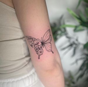 Elegant fine line and illustrative tattoo by artist Tom Boxell, featuring a delicate butterfly and intricate flower design.