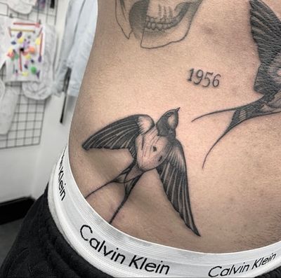 Tom Boxell's black and gray illustrative masterpiece captures the grace and beauty of a swallow bird in this stunning tattoo design.