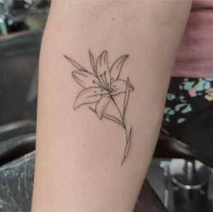 Adorn your skin with a delicate lily flower in fine line style by Tom Boxell, adding a touch of sophistication to your body art.
