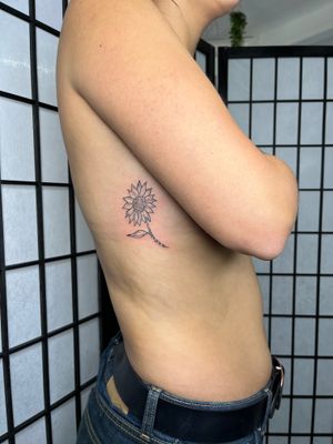 A beautiful floral and fine line illustrative tattoo of a sunflower, meticulously crafted by the talented artist Emily Bonnet.