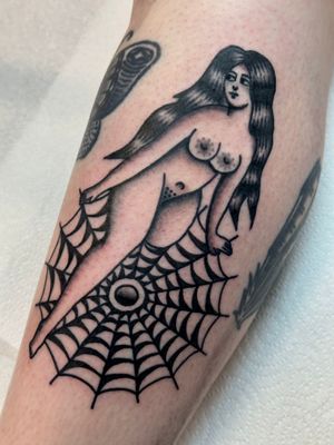 Get inked with a classic pin-up girl entwined in a spiderweb, expertly crafted by tattoo artist Jakob Isaac.