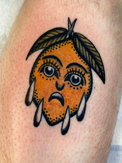 Vibrant traditional tattoo of an orange with a face, skillfully done by artist Jakob Isaac.