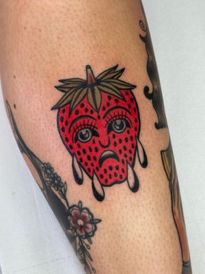 Vibrant traditional tattoo featuring a strawberry motif intertwined with a detailed face portrait by artist Jakob Isaac.