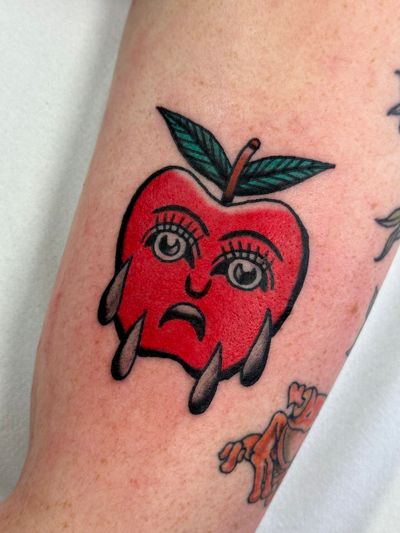 Get inked with this vibrant traditional style tattoo of a juicy apple merged with a mysterious face, designed by Jakob Isaac.