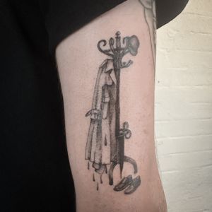 Unique and creative tattoo featuring a coat hanger and coat rack motif, designed by Jenny Dubet.