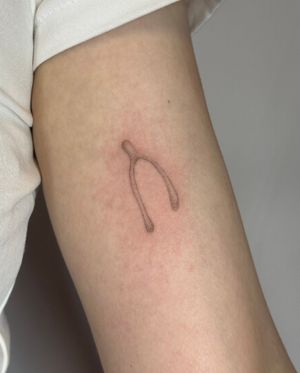 Experience the delicate artistry of dotwork and micro realism by Alina Wiltshire in this unique hand-poked wishbone tattoo.