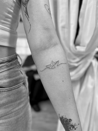Elegant fine line tattoo of a paper boat by Aleks Fanta. Intricate design with a delicate touch.