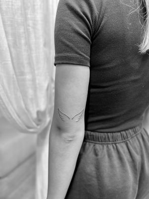 This fine line tattoo features delicate wings in a minimalistic style by the talented artist Aleks Fanta.