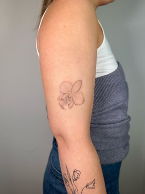 Experience the delicate beauty of a micro-realism orchid tattoo created through hand poke dotwork technique by talented artist Alina Wiltshire.