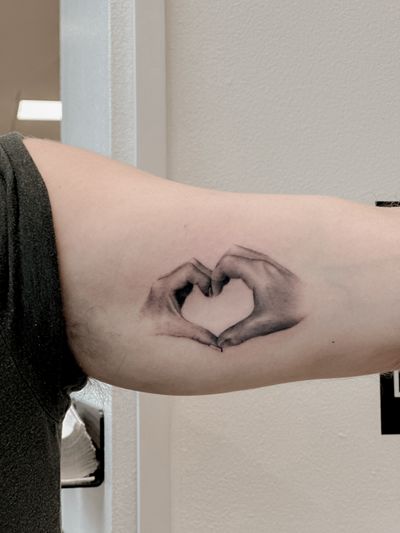 Black and gray micro realism tattoo of a heart held by hands, done by Carolina Feodorov.