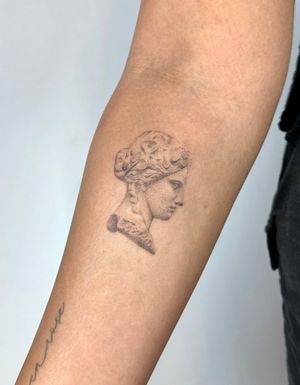 Experience a unique blend of realism and dotwork in this exquisite hand-poked statue tattoo by Alina Wiltshire.