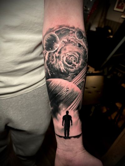 Get lost in the beauty of space with this black and gray illustrative tattoo featuring a galaxy, planets, and Saturn on a man's skin. Expertly done by artist Alex Santo.