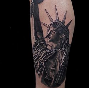 Realistic tattoo by Craig Hicks showcasing iconic Statue of Liberty in black and gray tones.