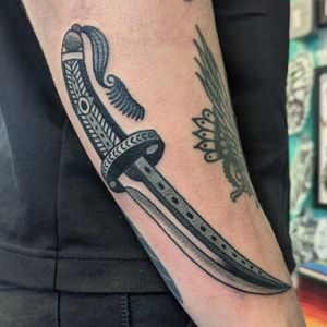 Get inked with a sharp and bold traditional knife design by the talented artist Benji Charnock. Make a statement with this timeless tattoo.