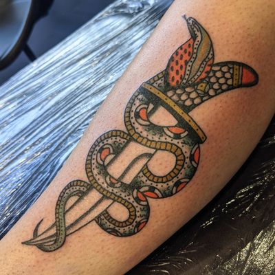 Get a classic tattoo by Benji Charnock featuring a fierce snake and sharp dagger in traditional style.