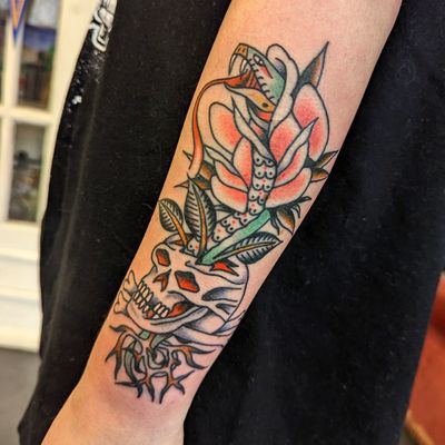 Get an edgy and bold traditional tattoo of a snake wrapped around a skull by artist Benji Charnock. Perfect for those who love classic tattoo motifs.